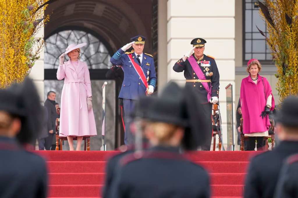 Крал Филип в униформа и кралица Матилда в елегантно палто стоят до крал Харалд V и кралица Соня пред двореца в Осло.