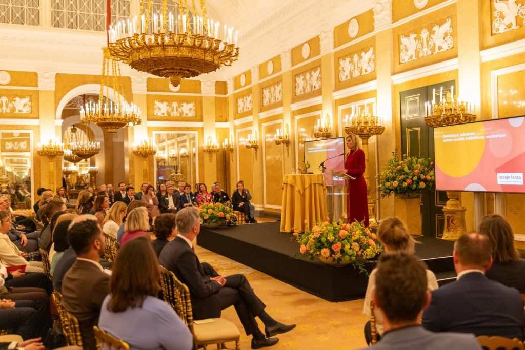 Кралица Максима произнася реч в салон, пълен с хора.