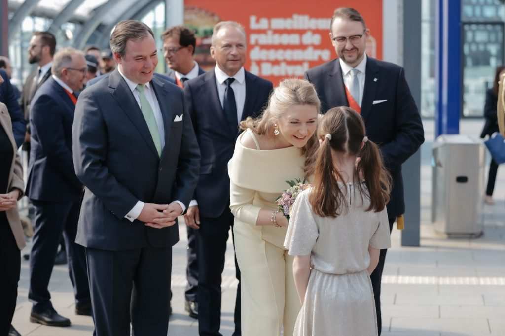 Великата херцогиня Стефания се е навела с усмивка към малко момиче, което ѝ подарява букет с цветя по време на официалното посещение в Еш-сюр-Алзет.