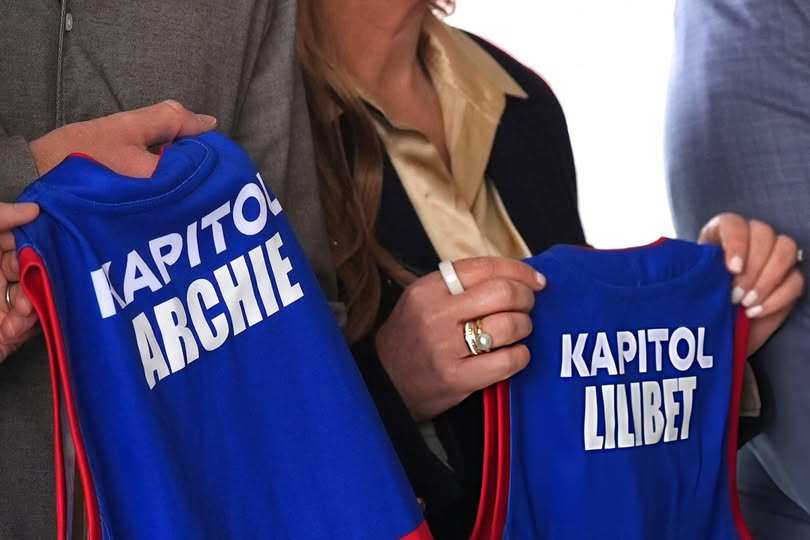 Принц Хари държи два малки спортни екипа в синьо и червено, на които пише „Archie“ и „Lilibet“.