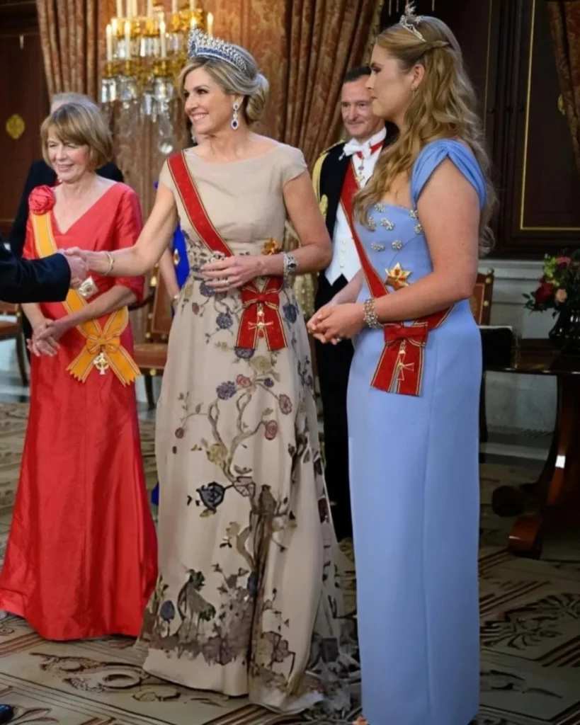 Трите дами в дълги рокли позират в официална зала. 